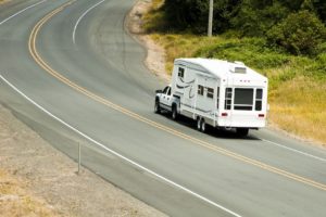 Truck hauling a fifth wheel trailer around a curved road.